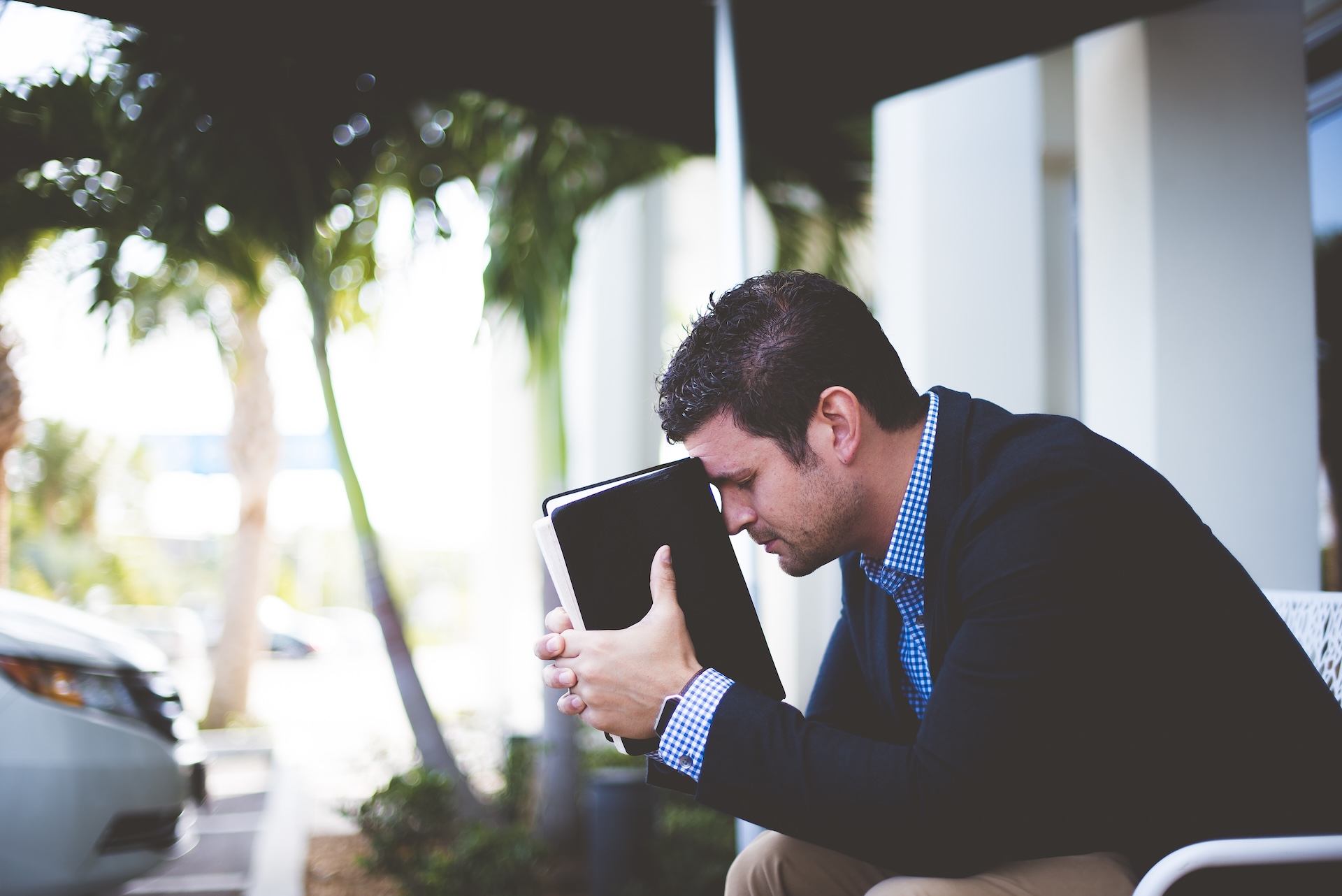Closeup shot well dressed male sitting while holding bible against his head